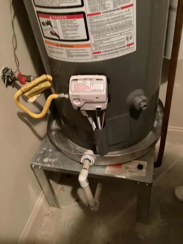 Tank water heater on a stand with a water-stained floor below after a leak